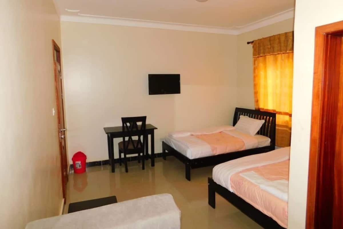 A room with two beds, a desk, a chair, a television, and a door.