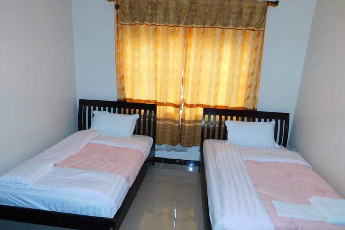 A room with two single beds, a window with curtains, and a tiled floor.