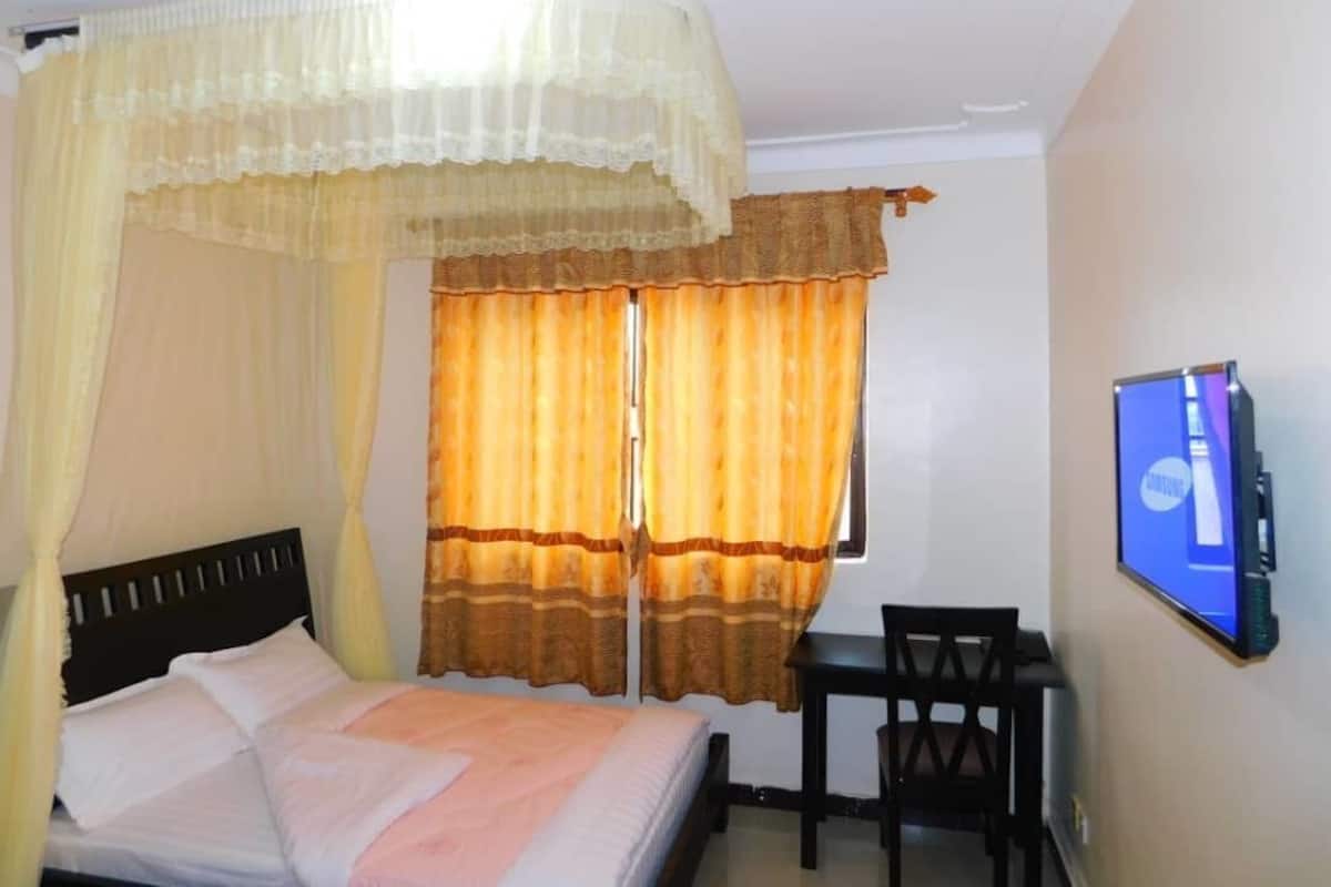 A room with a bed, a desk, a chair, a TV, and a window with curtains.