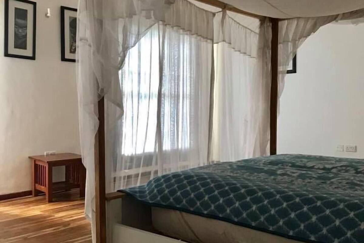 A room with a four-poster bed, wooden flooring, and a small side table.