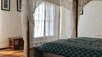 A room with a four-poster bed, wooden flooring, and a small side table.