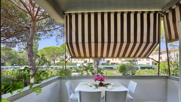 A balcony with a striped awning, white chairs, and a table with a vase of flowers. - Case Sobrini (Rosignano Marittimo)