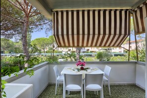 A balcony with a striped awning, white chairs, and a table with a vase of flowers. - Case Sobrini (Rosignano Marittimo)