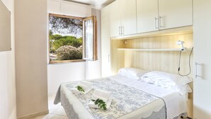 A bedroom with a bed, a window with a view of greenery, and a bedside table with a lamp. - Case Sobrini (Rosignano Marittimo)