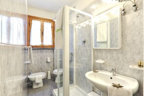 A bathroom with a glass-enclosed shower, a sink, a toilet, and a mirror.