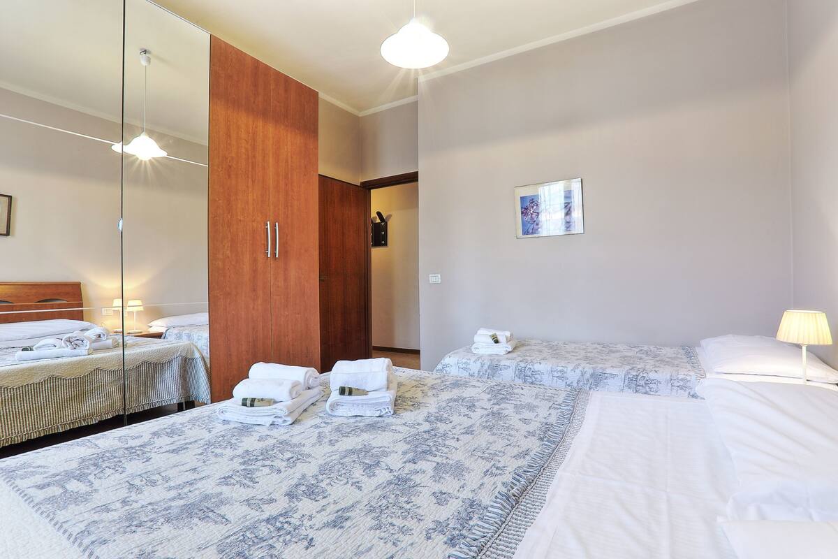 A hotel room with two beds, a wooden wardrobe, a mirror, and a framed picture on the wall.