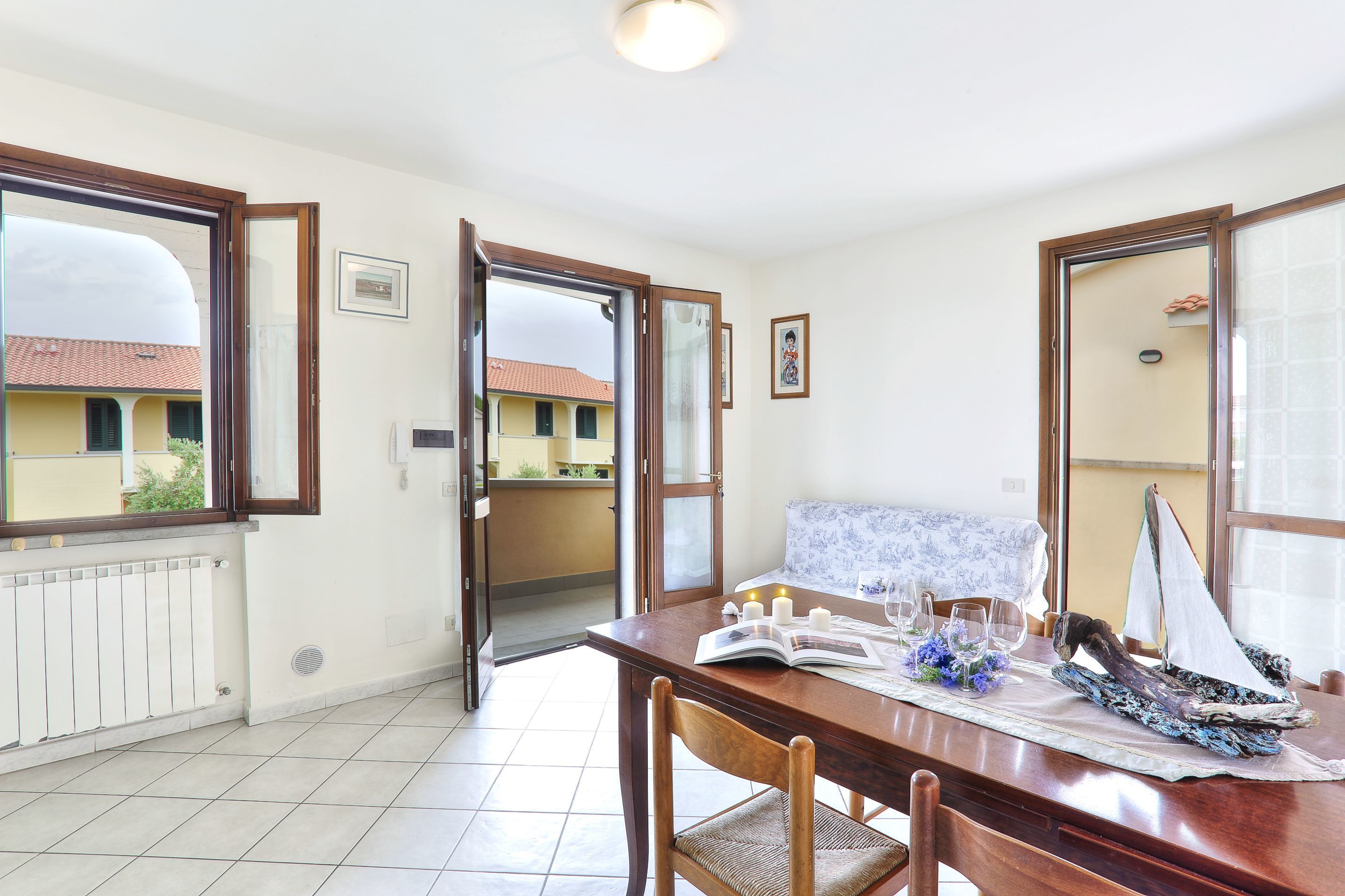 Comedor con mesa de madera, sillas y vistas a un balcón desde una puerta abierta.