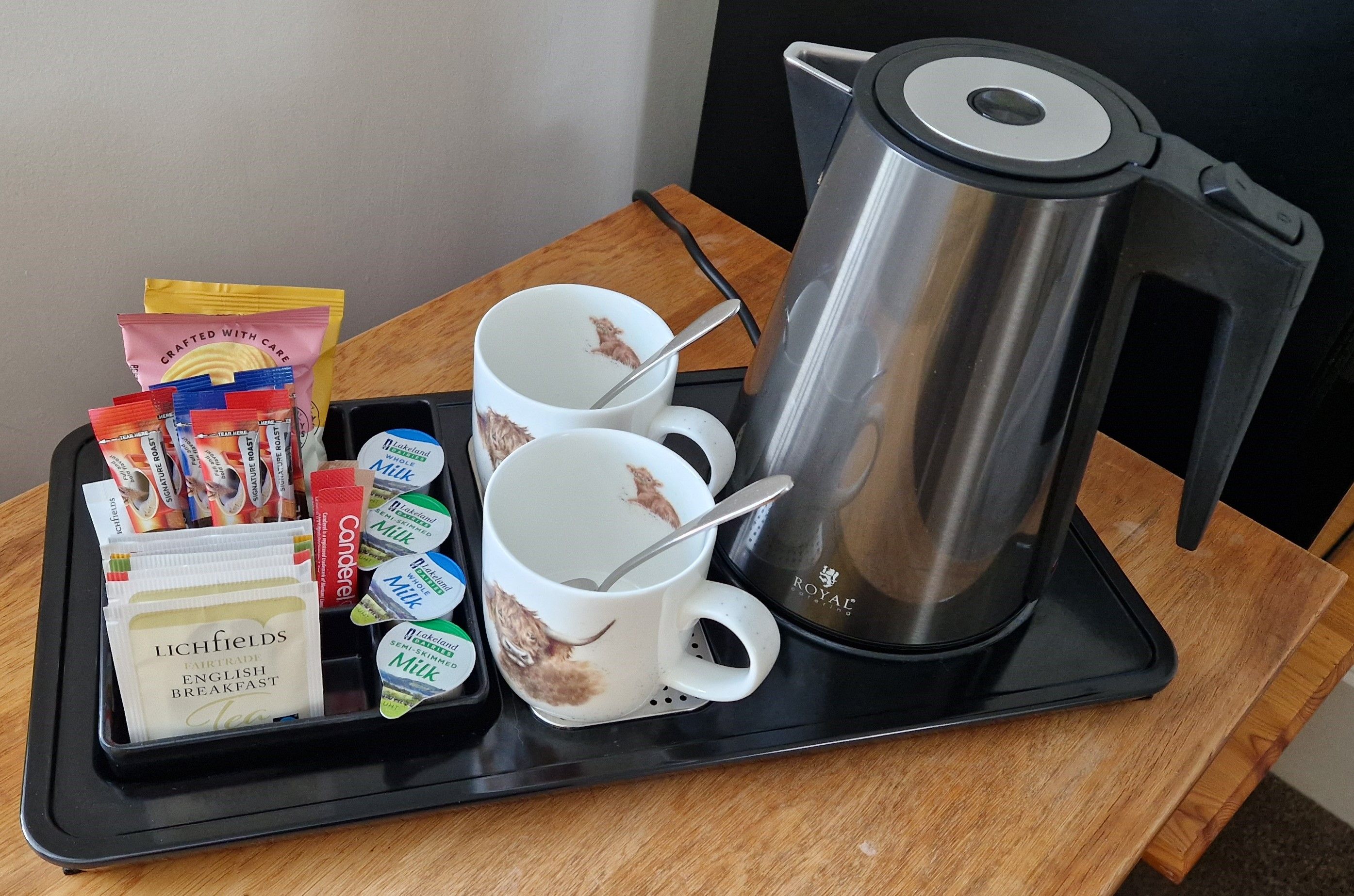 Un plateau avec une cafetière, deux tasses et divers éléments pour le petit-déjeuner, notamment des sachets de thé et des briques de lait.