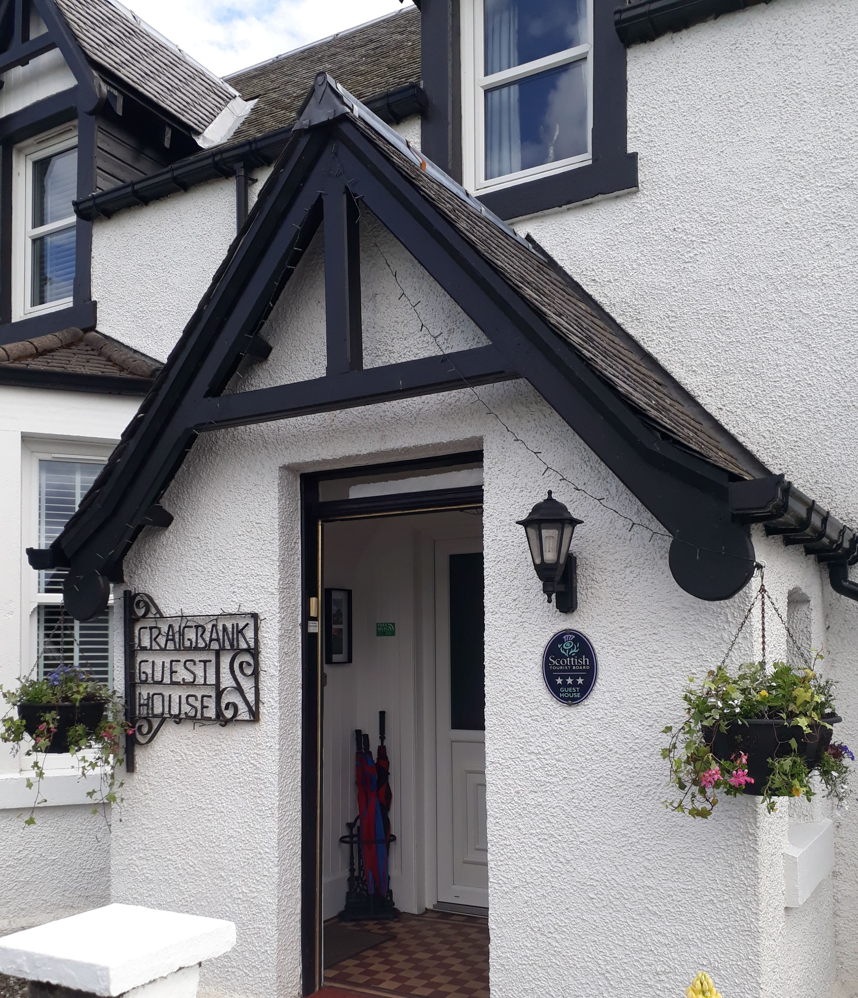 A white building with a black roof and a sign reading "CRAGBANK GUEST HOUSE".