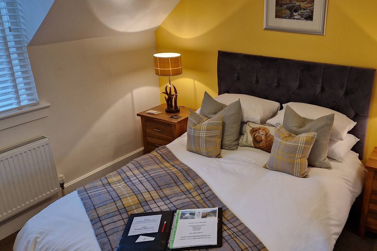 A neatly made bed with a plaid blanket, two bedside tables with lamps, and a framed picture on the wall.