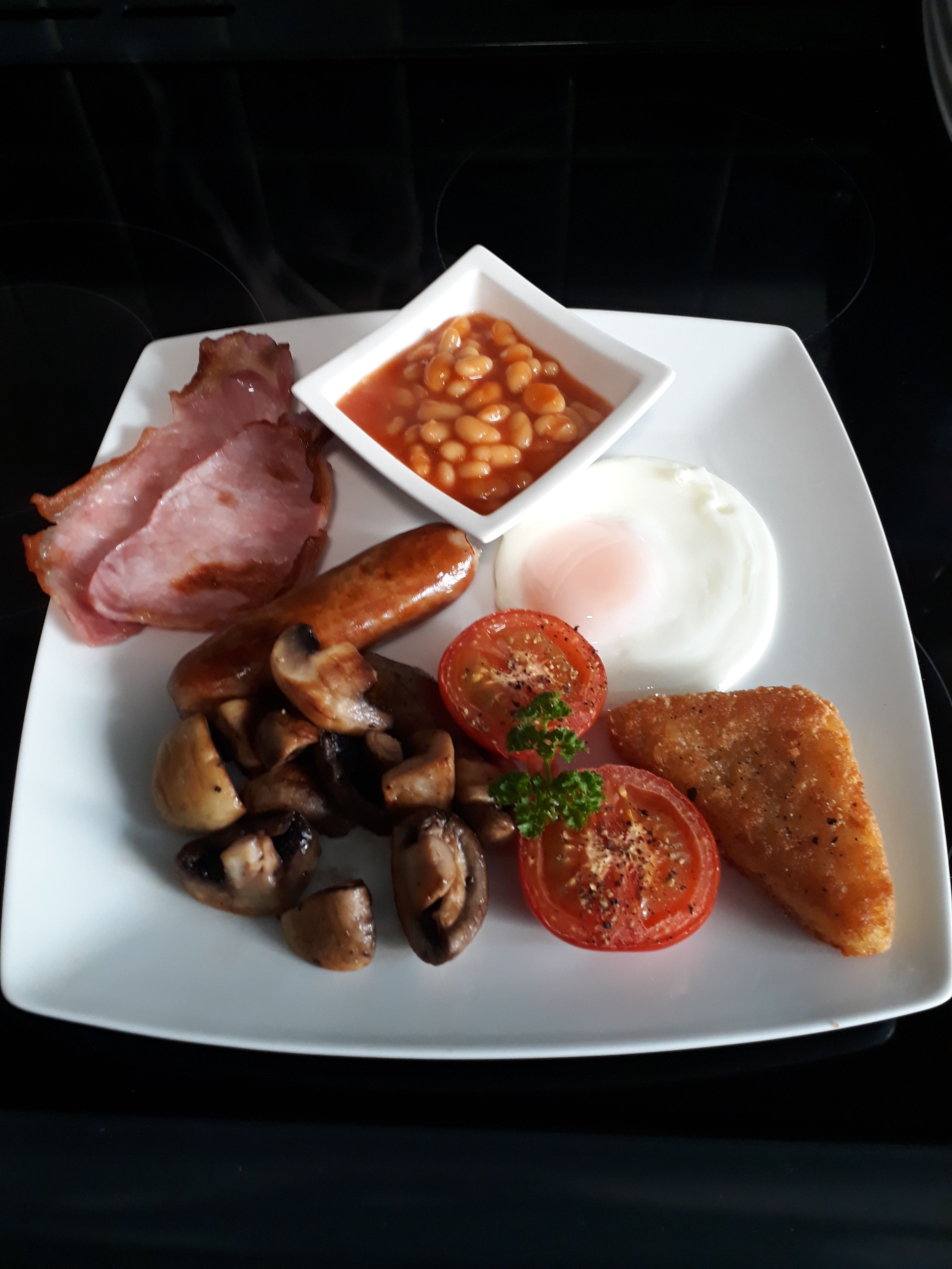 A plate of food including bacon, eggs, mushrooms, tomatoes, and beans.