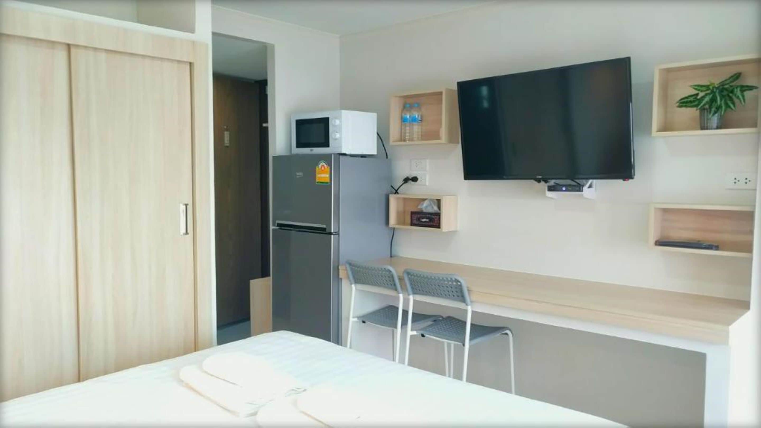 A compact hotel room with a bed, a desk with two chairs, a flat-screen TV, a refrigerator, and a microwave.