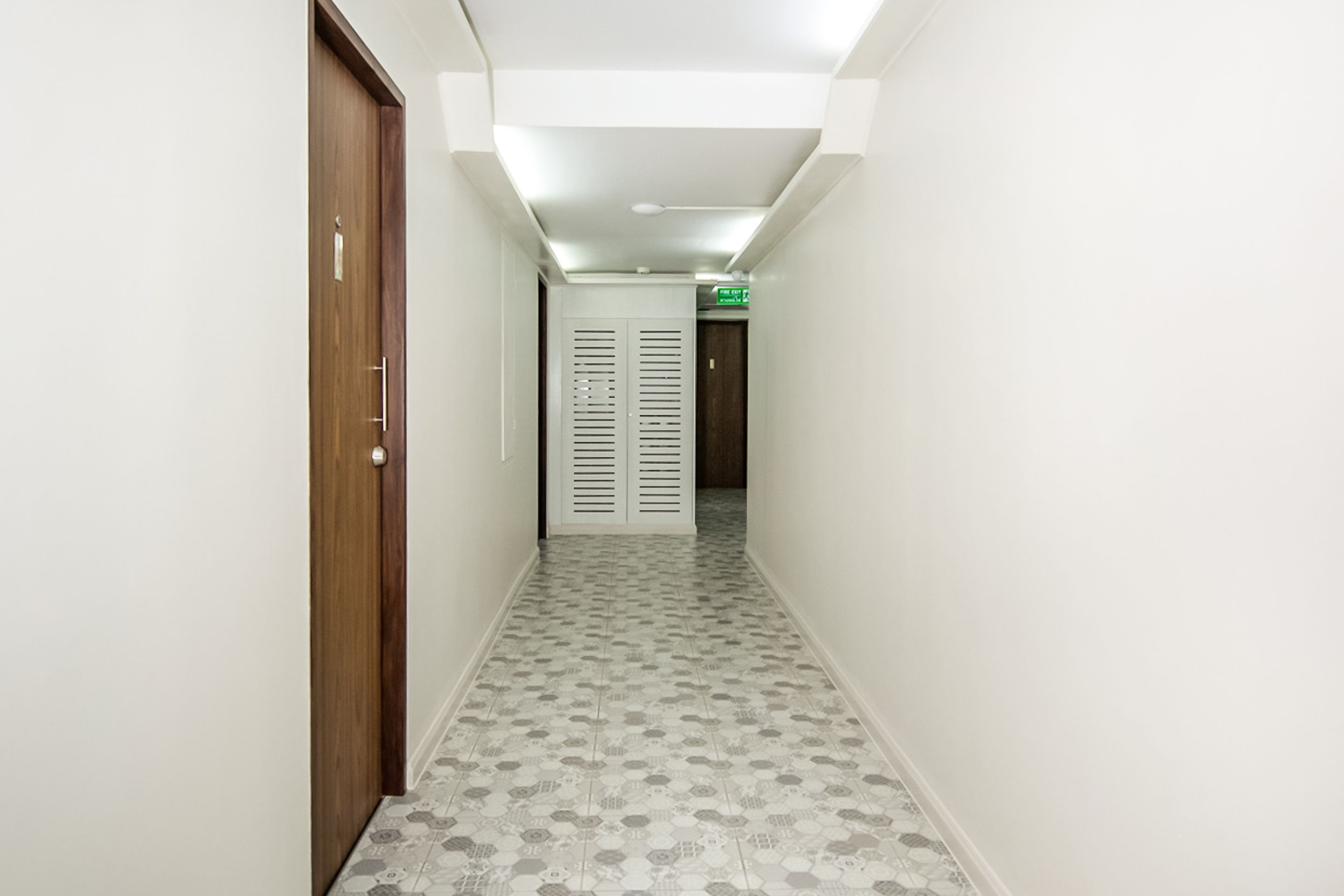 Un pasillo estrecho con baldosas de diseño, una puerta de madera a la izquierda y una puerta blanca al final.