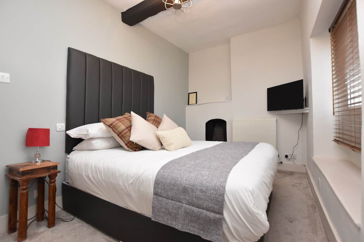 A bedroom with a bed, a bedside table with a lamp, a television on the wall, and a radiator.