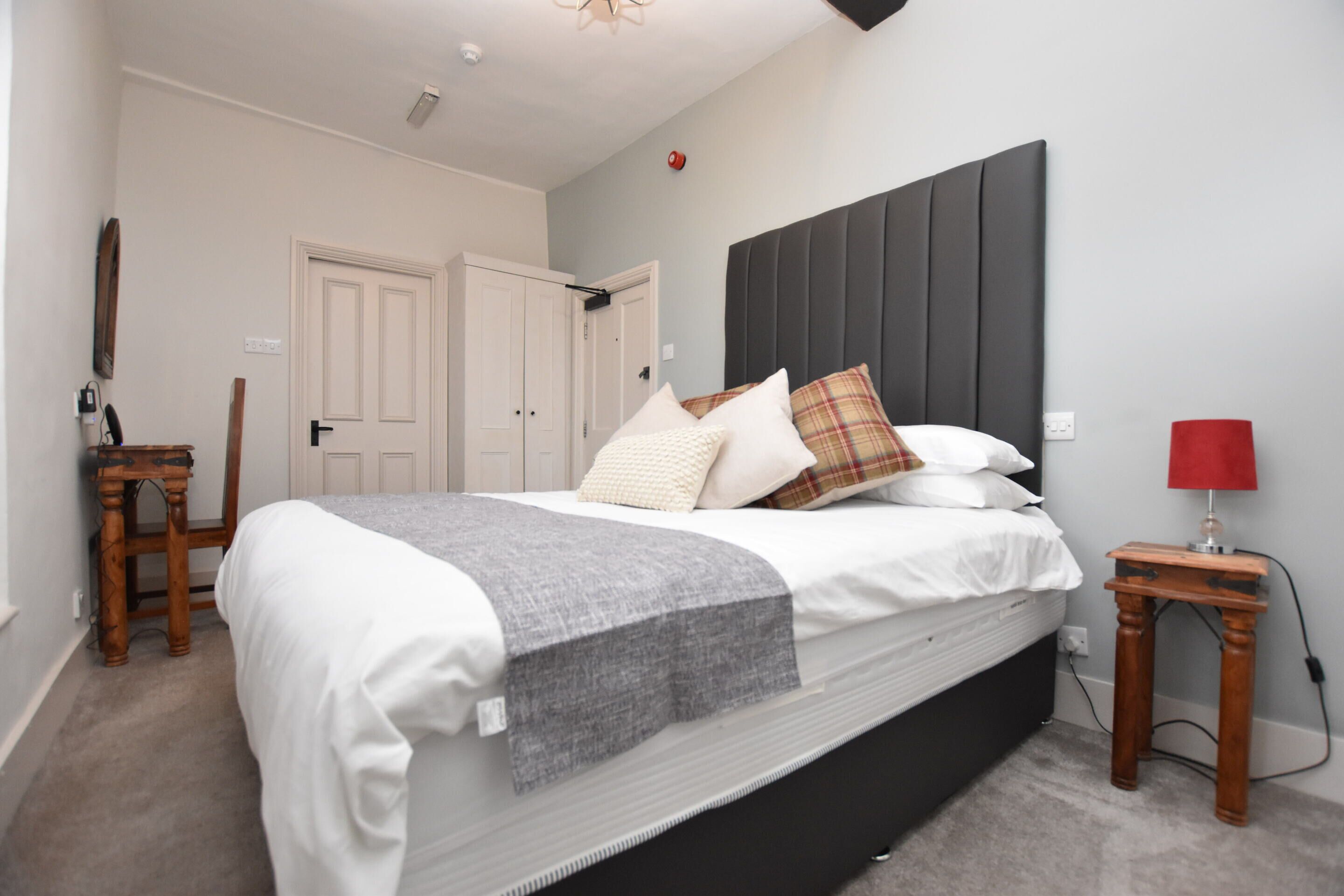 A bedroom with a bed, a bedside table, a chair, and a door.