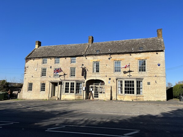A stone building with a flag, a sign, and a statue in front. - The Halford Bridge Inn (Shipston on Stour)