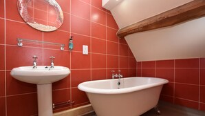 Une salle de bain avec des murs recouverts de carreaux rouges, un lavabo blanc et une baignoire blanche sur pieds.