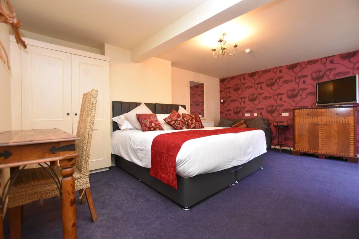 A bedroom with a bed, a desk, a chair, a television, and a wardrobe.
