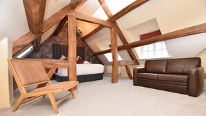 Une chambre à coucher aménagée dans un grenier, avec un plafond en pente, des poutres en bois, un lit, un canapé en cuir marron et une chaise en bois.