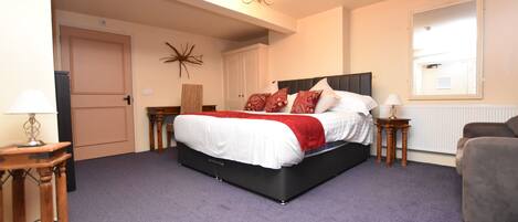 A bedroom with a large bed, a nightstand, a chair, and a door.