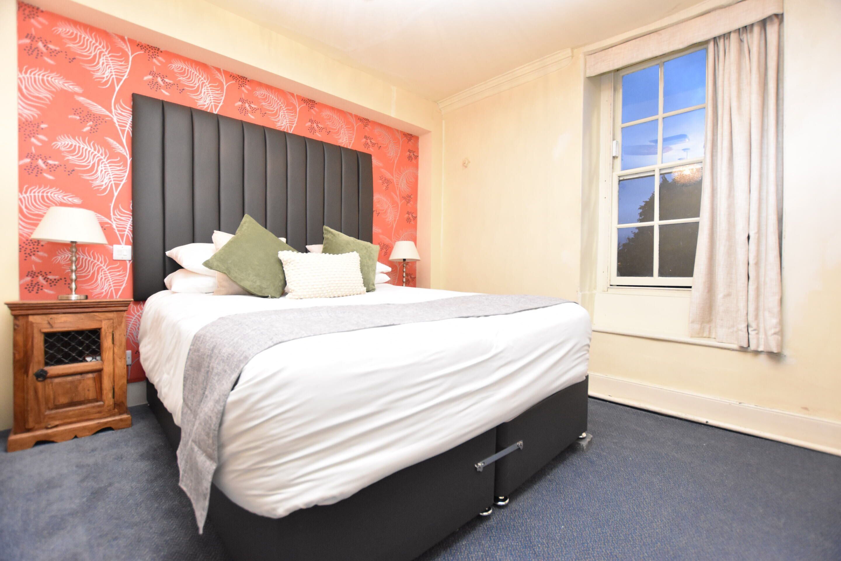 A neatly made bed with a headboard, two bedside tables with lamps, and a window with curtains.