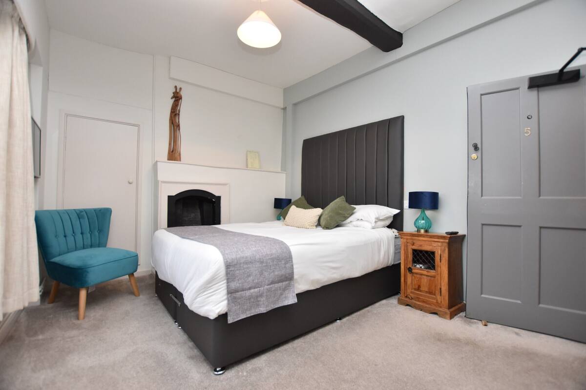 A bedroom with a bed, a chair, a nightstand, and a door.