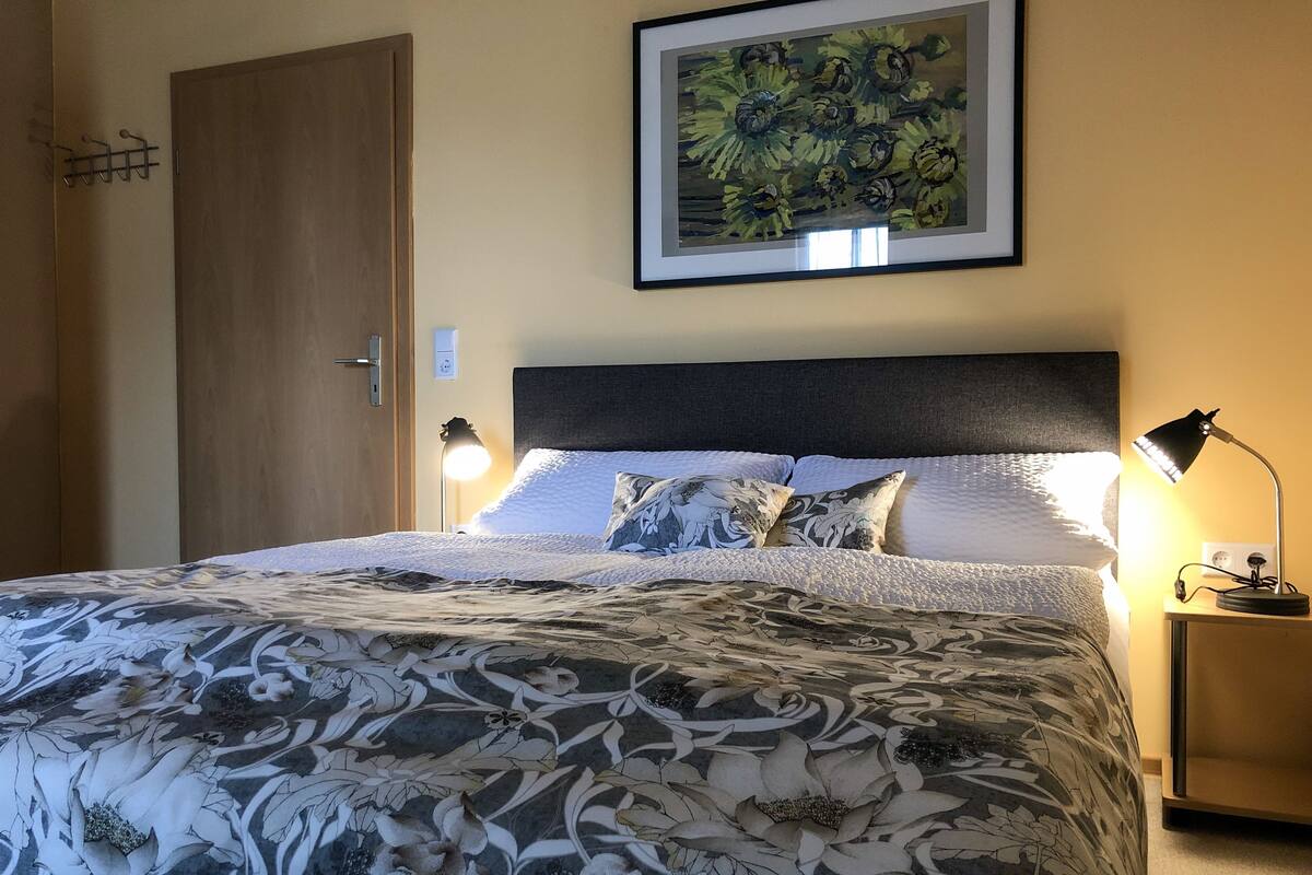 A neatly made bed with a floral-patterned bedspread, a dark headboard, and two bedside lamps.