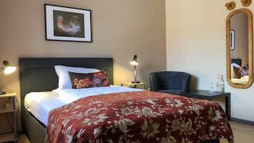 Una camera d'albergo ordinata con un letto, lampade sui comodini, una sedia, un tavolino e uno specchio, oltre a un quadro appeso al muro.