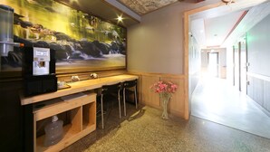 Un restaurant avec un comptoir en bois, des chaises noires, une machine à café et une fresque murale représentant une cascade.