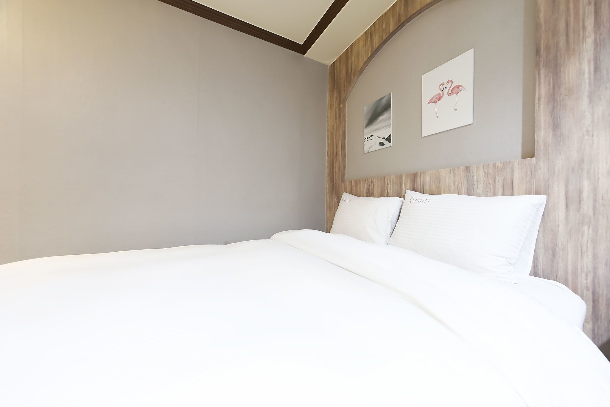 Una cama bien tendida en una habitación de hotel, con cabecera de madera y dos cuadros en la pared.