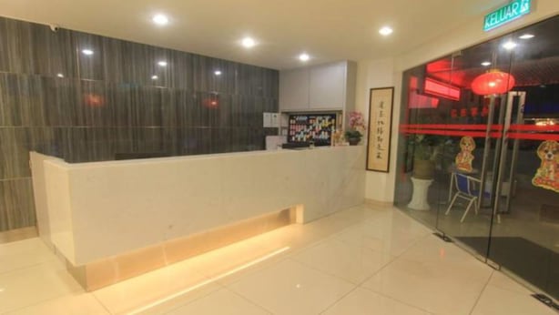 A reception area with a modern design, featuring a reception desk, a wall-mounted display, and a glass door leading to a brightly lit interior.