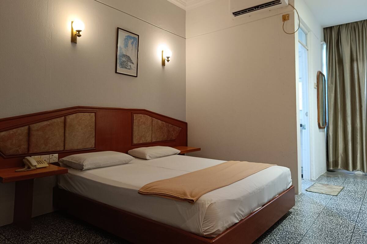 Habitación de hotel con cabecera de madera, dos mesitas de noche, un teléfono, un cuadro en la pared y un equipo de aire acondicionado.