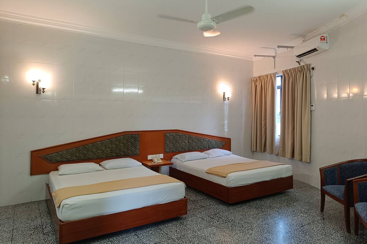 Habitación de hotel con dos camas, ventilador de techo, aire acondicionado montado en la pared y ventana con cortinas.