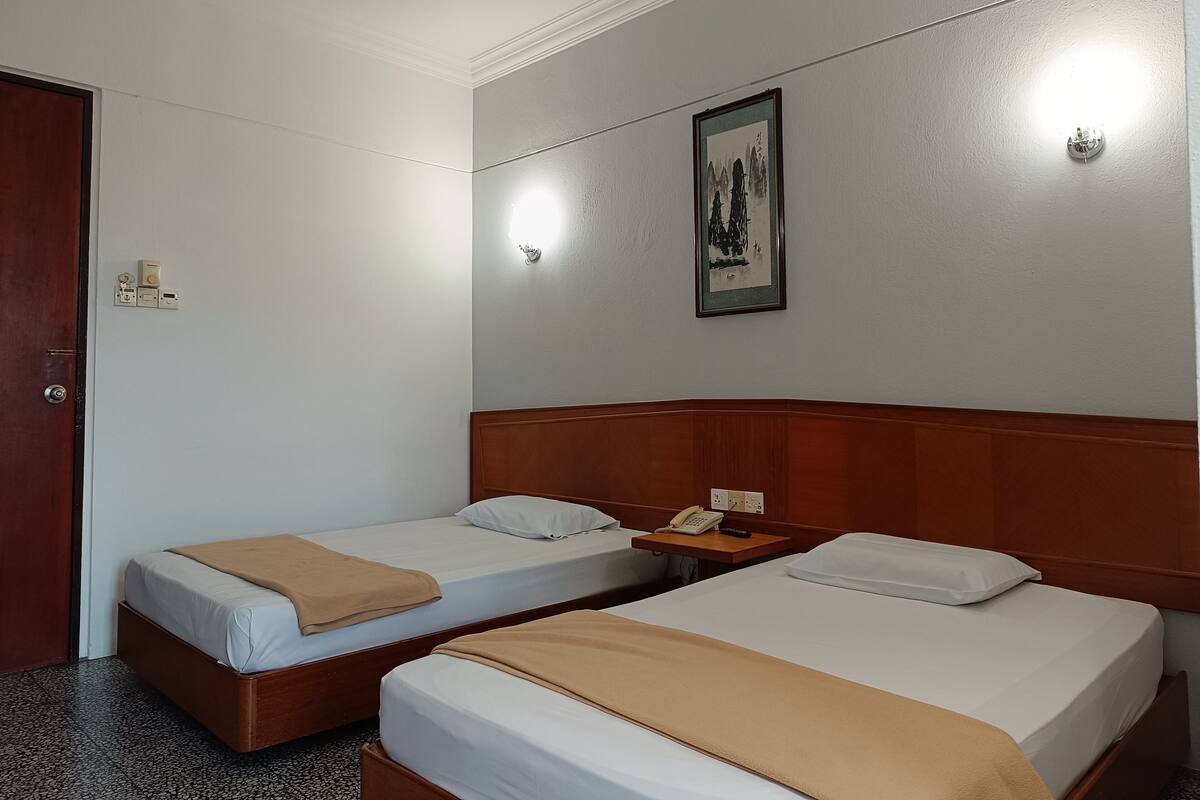 Una habitación de hotel con dos camas individuales, un cabecero de madera, una mesita de noche con un teléfono y una lámpara de pared.