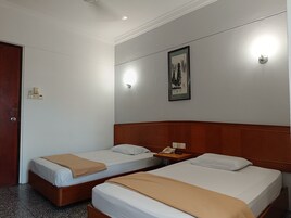 Una habitación de hotel con dos camas individuales, un cabecero de madera, una mesita de noche con un teléfono y una lámpara de pared.