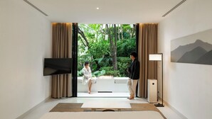 A modern hotel room with a large window, a flat-screen TV, a bedside table, and a lamp. - K Maison Lanna Boutique Hotel (Chiang Mai)