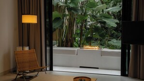 A modern room with a view of lush greenery, a comfortable chair, a floor lamp, and a small table with a tray. - K Maison Lanna Boutique Hotel (Chiang Mai)