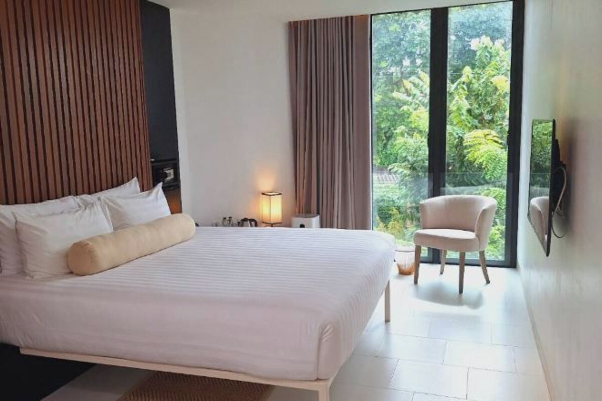 A modern bedroom with a large bed, a bedside table, a chair, and a TV mounted on the wall.