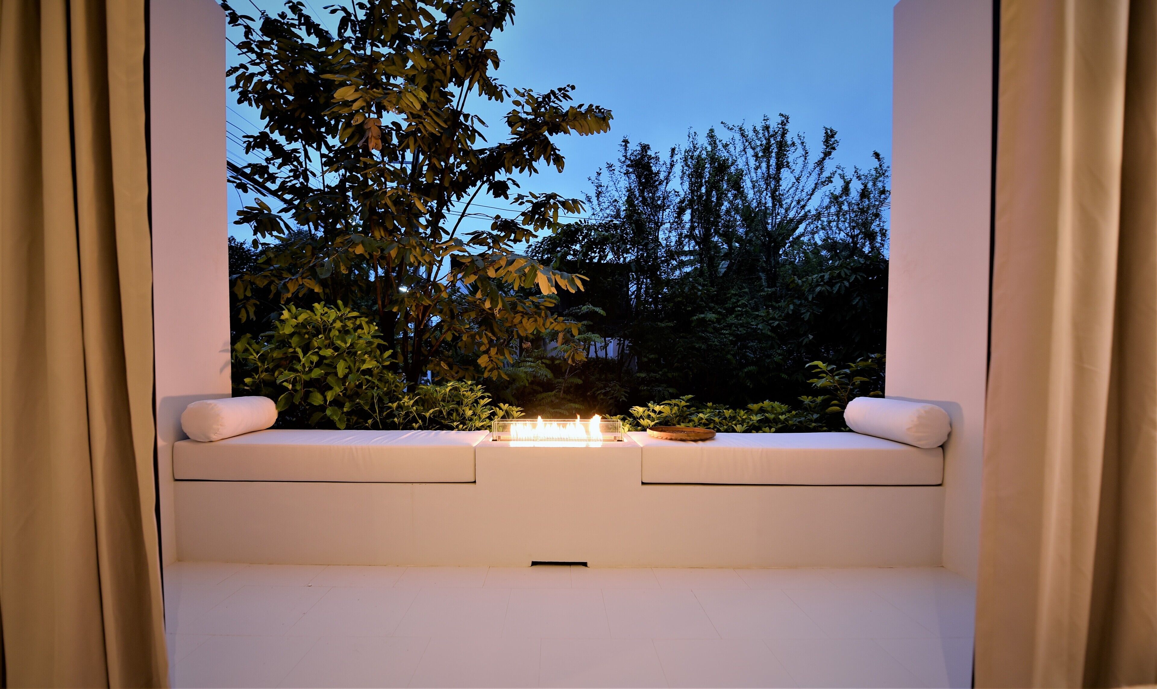 Una habitación con ventanal que da a un jardín al atardecer.