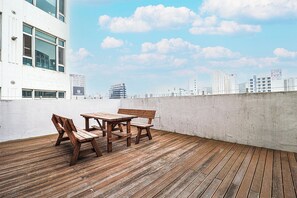 A rooftop terrace with wooden furniture and a city skyline in the background. - Browndot Hotel - Gold (Busan)