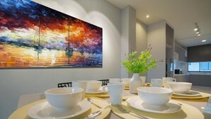 A modern dining area with a table set for four, a vibrant abstract painting on the wall, and a potted plant on the table.
