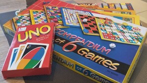 A variety of board games, including UNO and Monopoly, arranged on a carpeted floor.