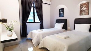 A hotel room with two single beds, a window with curtains, a vase with flowers, and a motivational quote on the wall.