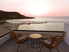 Un balcón con sillas de mimbre y una pequeña mesa redonda, con vista a una playa al atardecer.