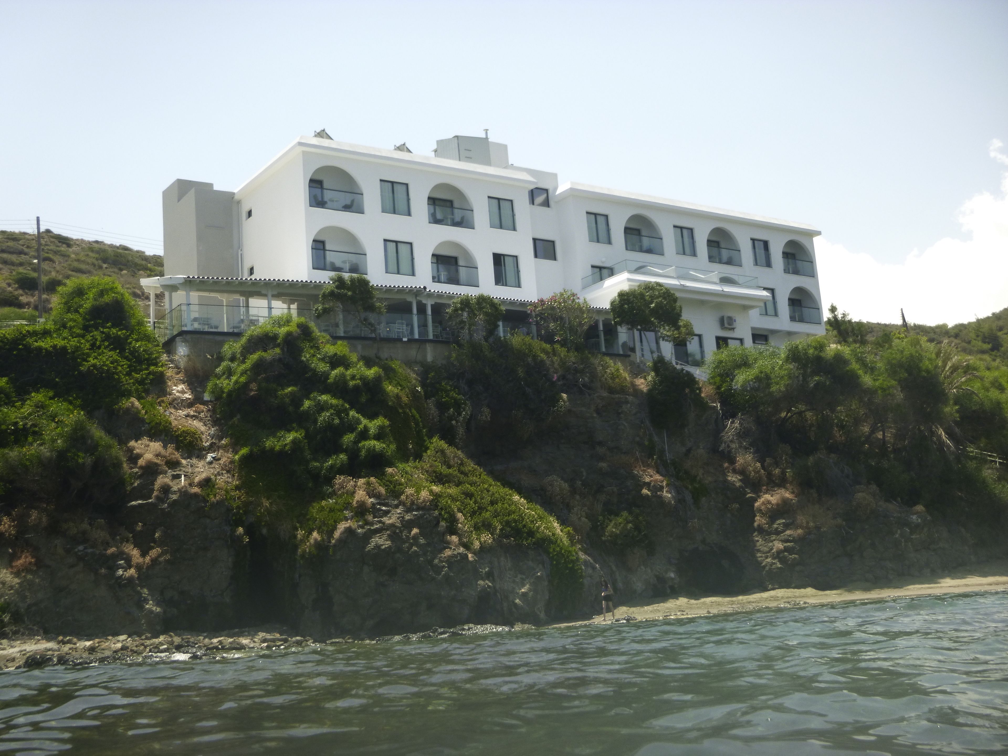 Un edificio blanco con varios balcones, ubicado en una ladera con vista a un cuerpo de agua.