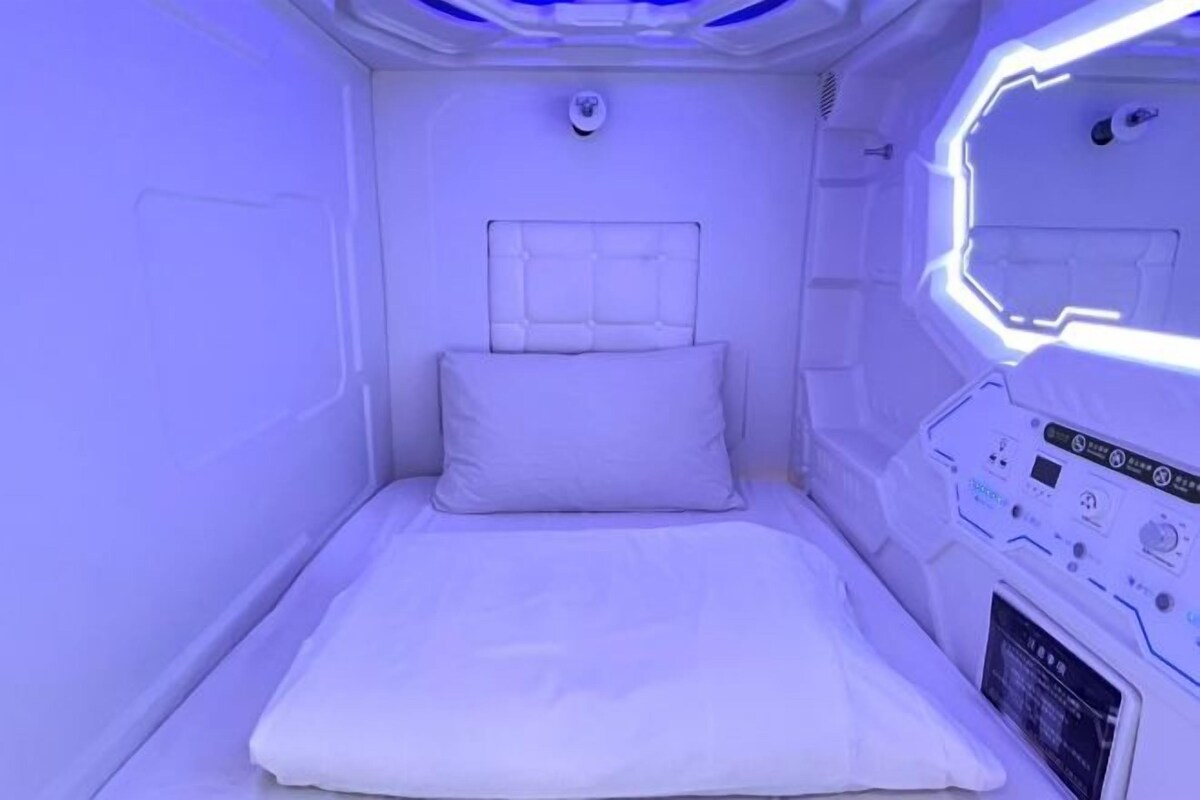 A small, private room with a bed, control panel, and a window.