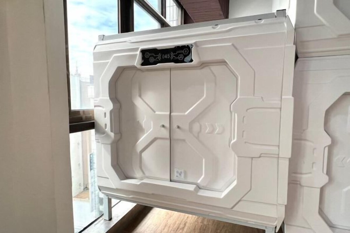 A white, modern-looking cabinet with a geometric design, placed in a room with a large window.