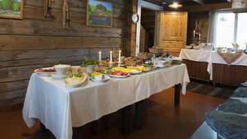 A wooden cabin interior with a dining table set for a meal, featuring various dishes and candles.