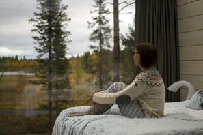 A person sitting on a bed with a view of a forest and a lake.