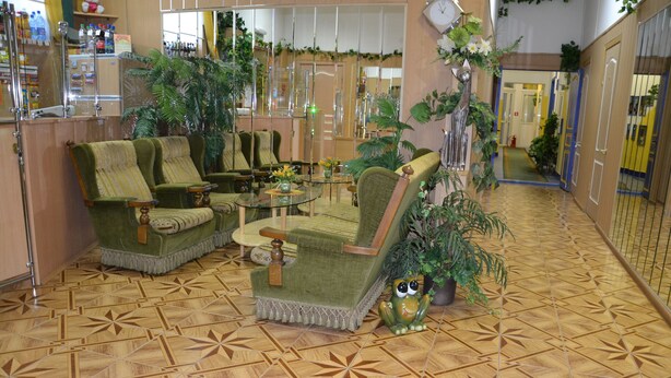 Un hall d’entrée doté d’un parquet à motifs, de fauteuils à revêtement vert, d’une table basse en verre et de diverses plantes en pot.